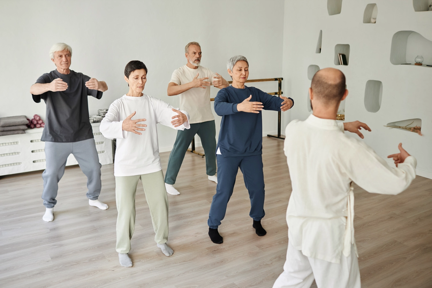 Chan tao - Institut für Gesundheit - Weitwinkelaufnahme älterer Menschen, die während einer Qigong-Übung im Fitnessstudio meditieren, während ein männlicher Trainer unterrichtet